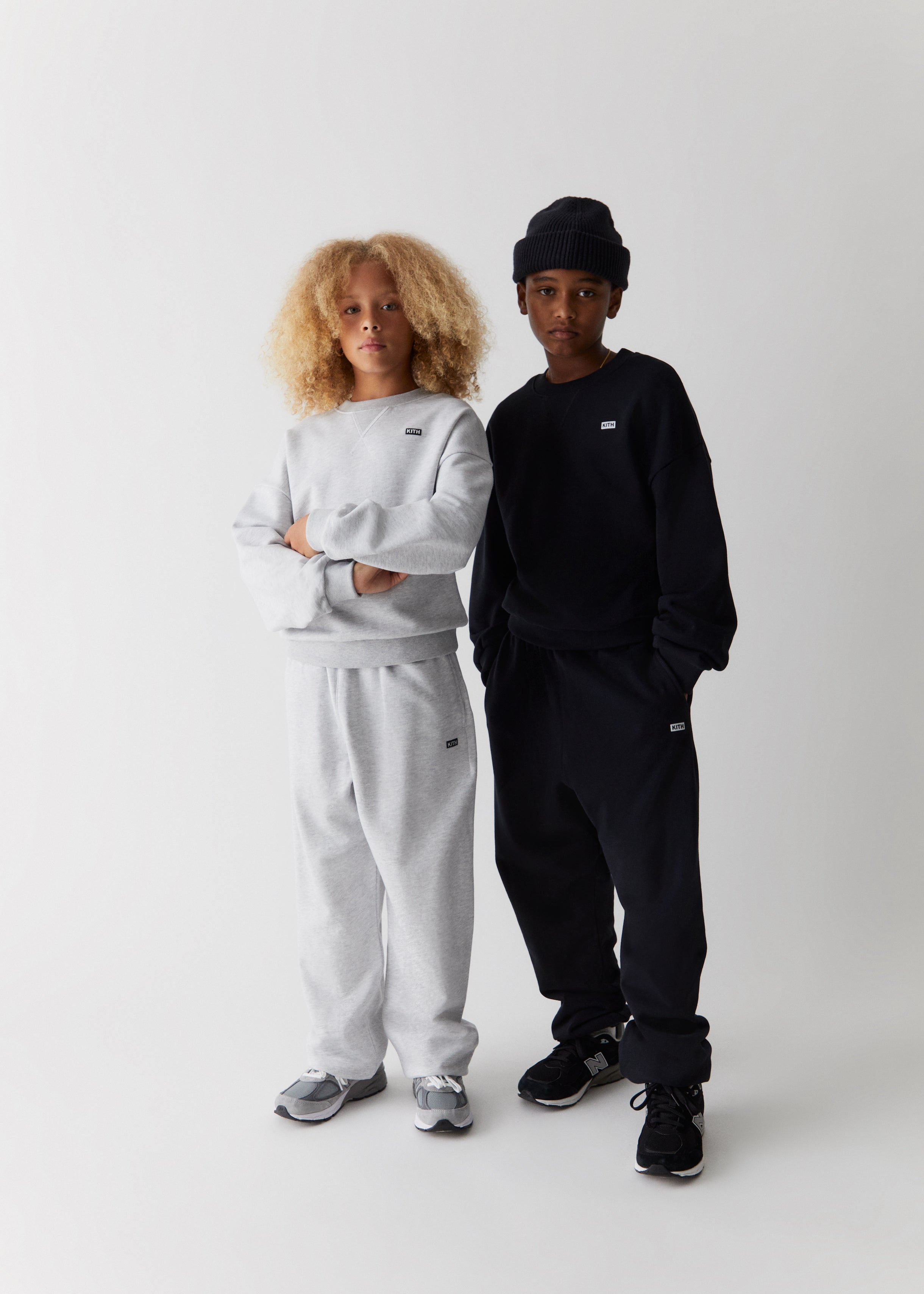Two children wearing crewneck sweatshirts and matching sweatpants in a grey and black shade form the Kith Kids Fall Classics 2023 collection.