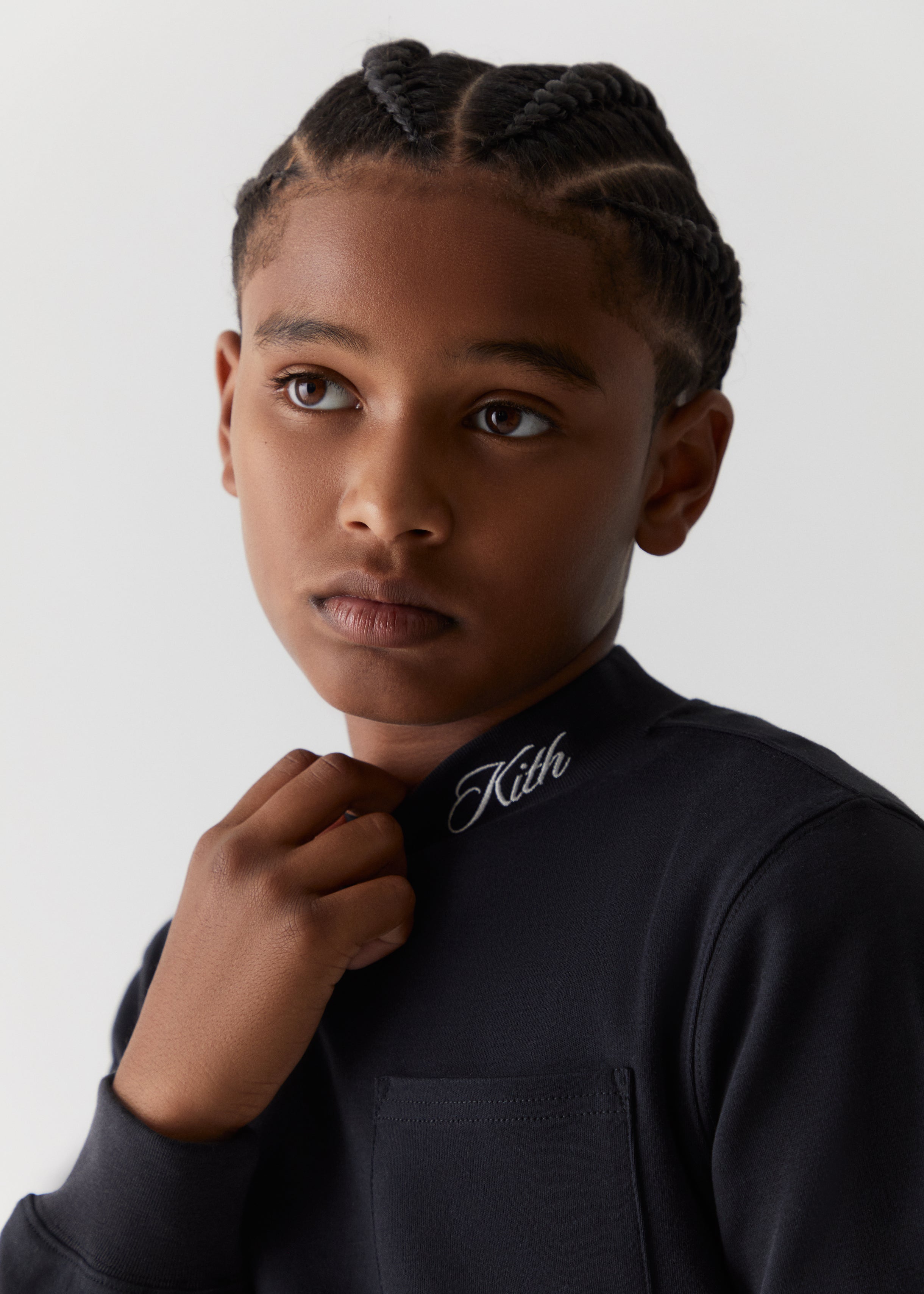 A child wearing a Kith-branded black turtleneck shirt from the Kith Kids Fall Classics 2023 collection.