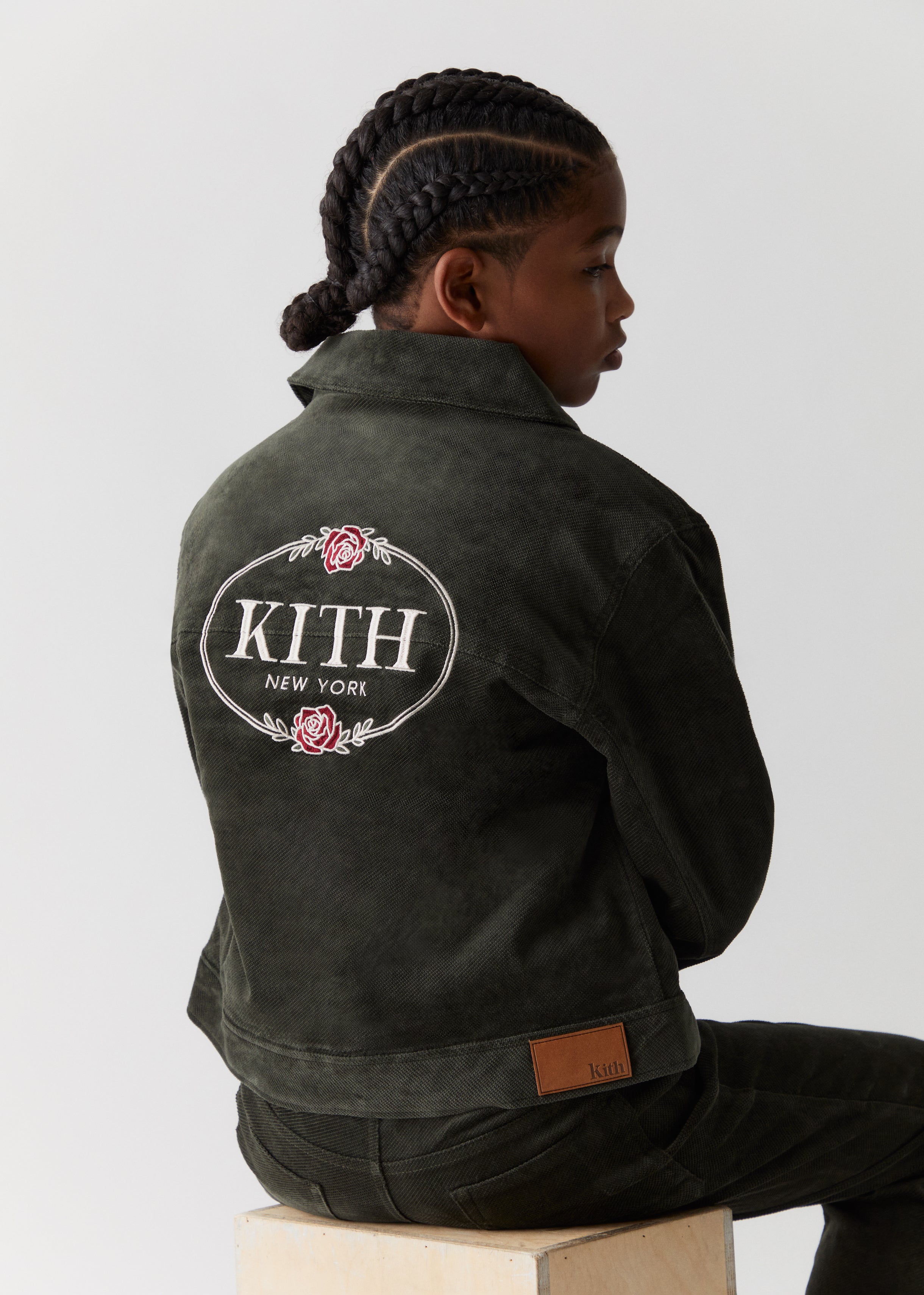 A child facing backwards wearing a green corduroy jacket with Kith embroidery on the back and matching green corduroy pants, all from the Kith Kids Fall Classics 2023 collection.